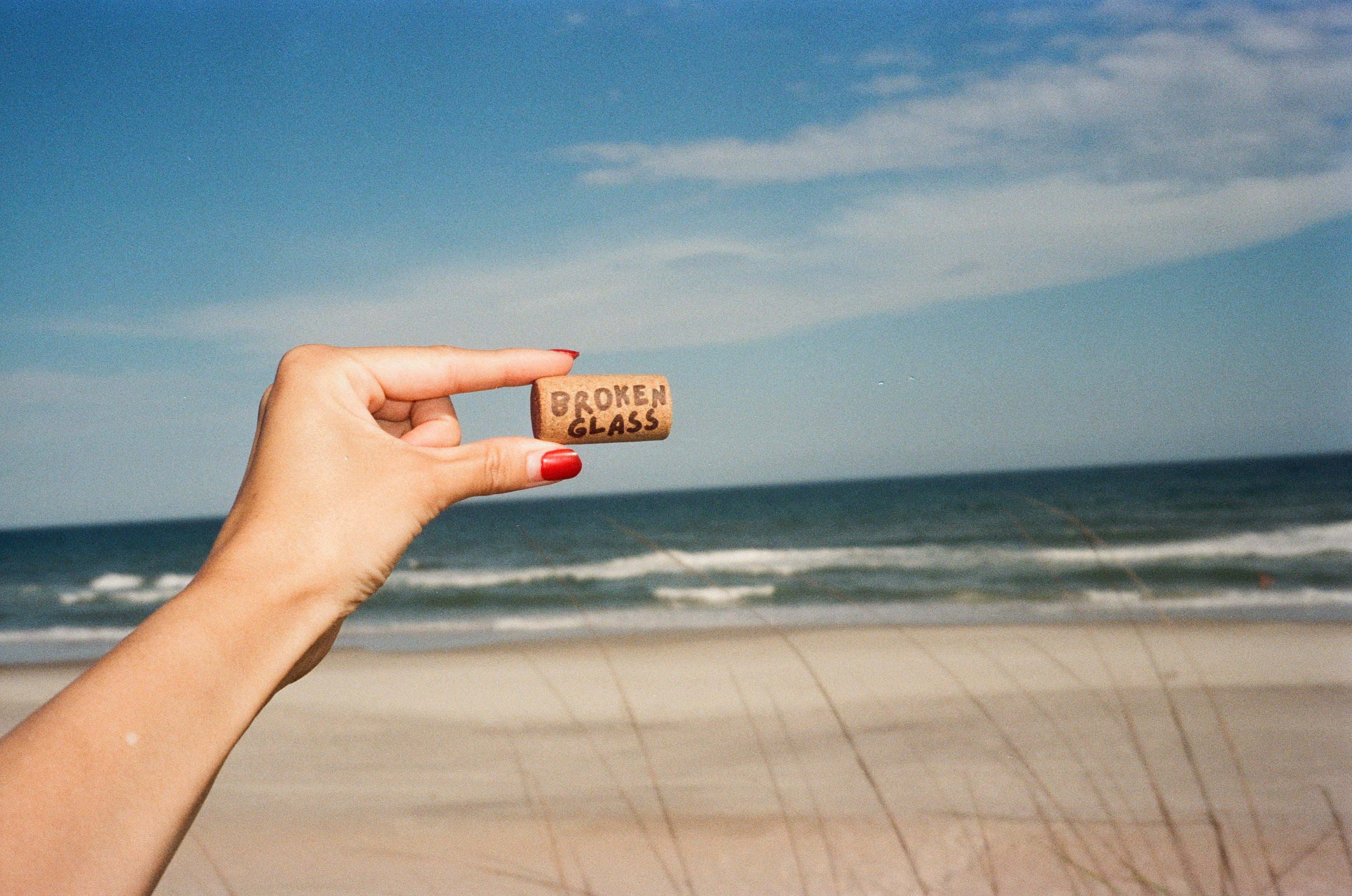 Hand holding a 'Broken Glass' cork by the ocean