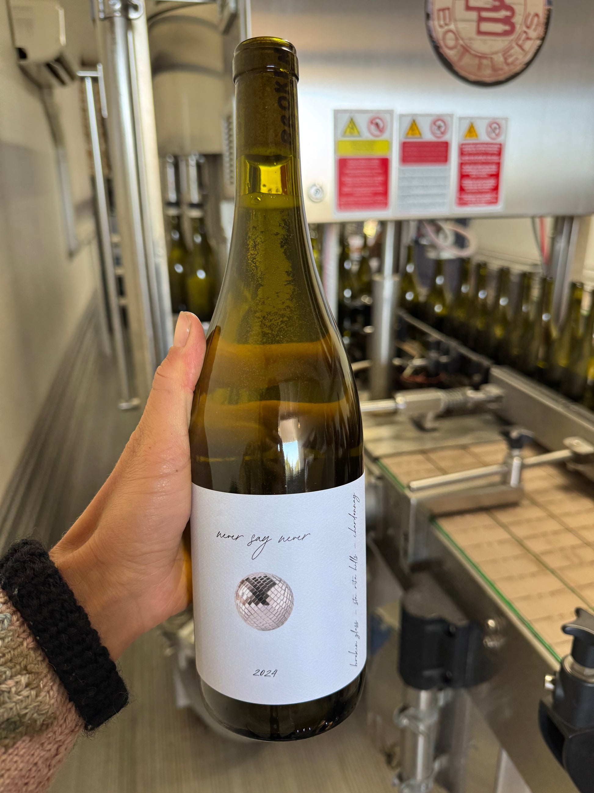 Person holding a wine bottle with a label in an industrial setting
